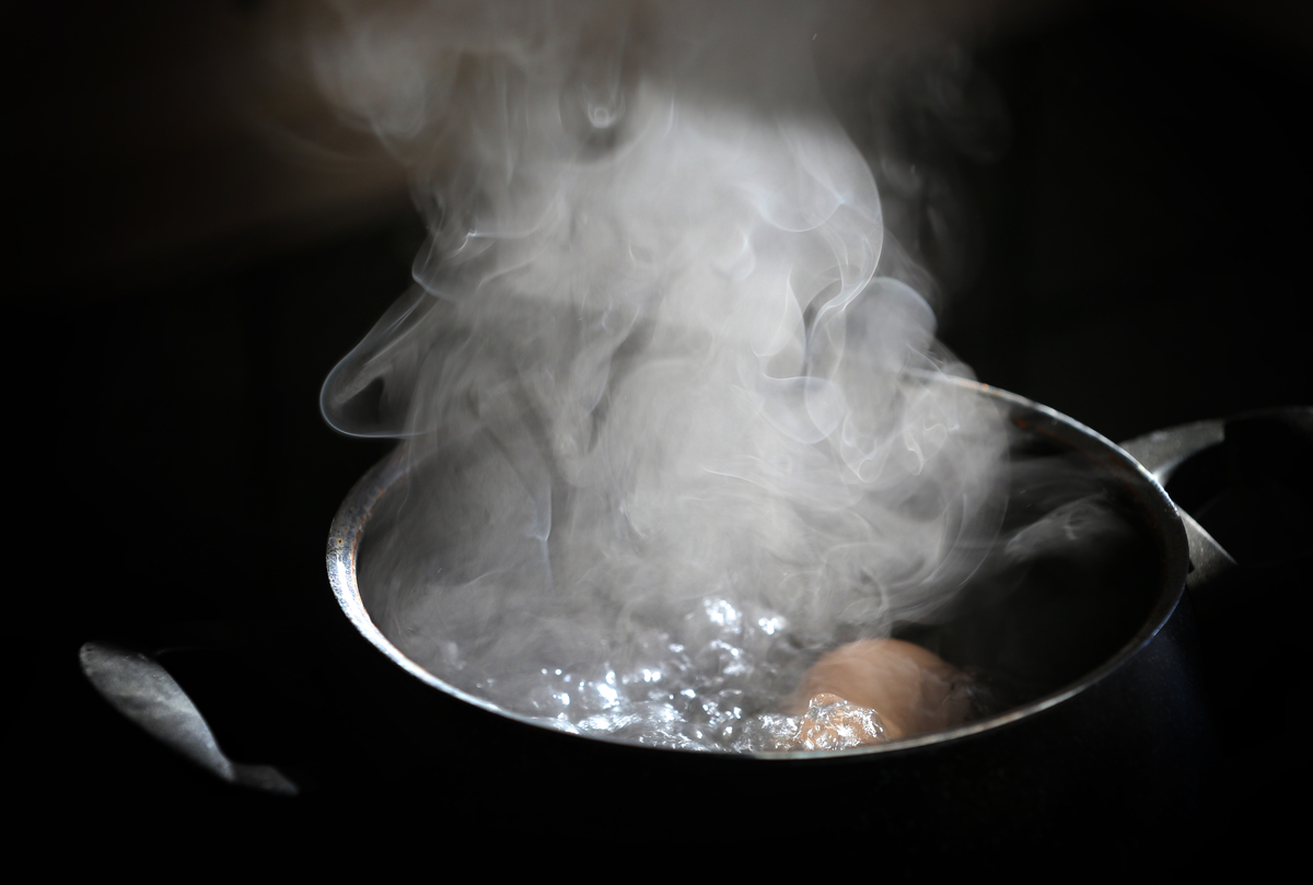 An egg lies in a pot on a hotplate in boiling water