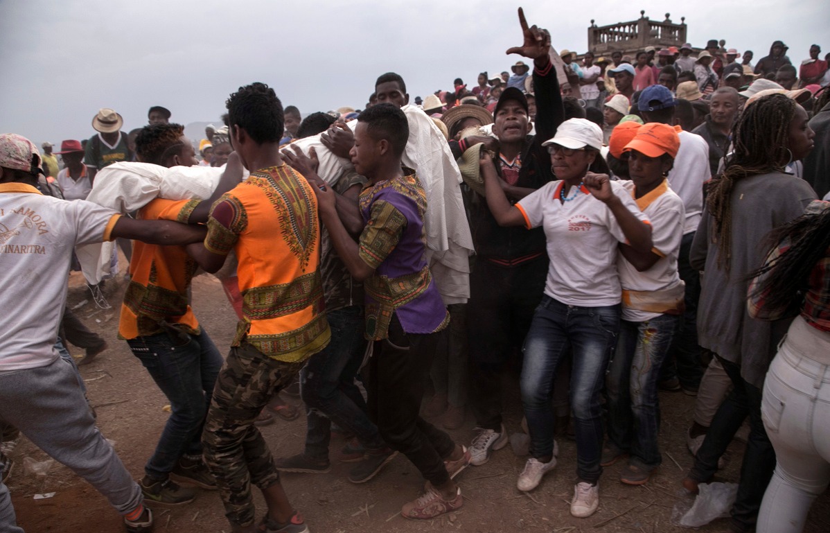 People dance and sing next to men carrying a body as they all take part in a funerary tradition called the Famadihana in the village of Ambohijafy