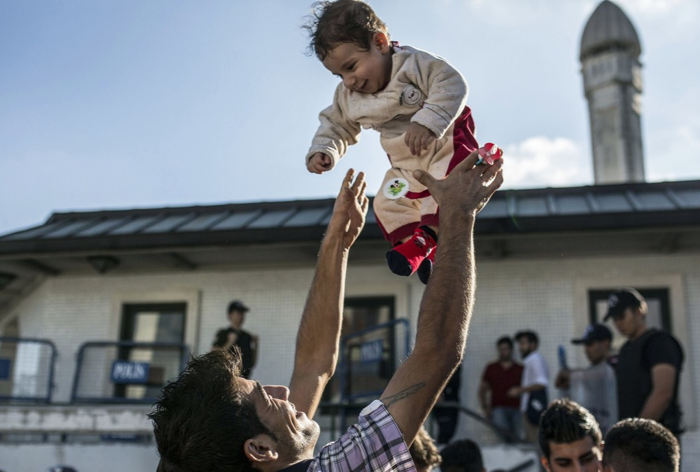 A migrant man throws his baby in the air at Istanbul's Esenler Bus Terminal while waiting for buses
