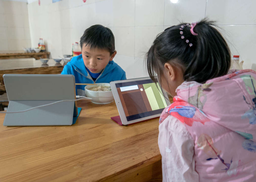 wo elementary school students watch cartoon video and play games on mobile device when having dinner.