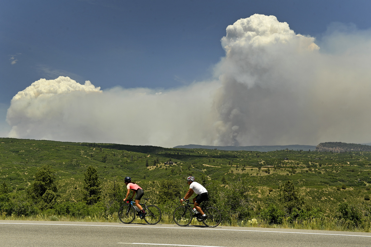 Cyclists look at the large plume of the 416 fire as they make their way up Highway 160 on June 12, 2018 near Hesperus, Colorado