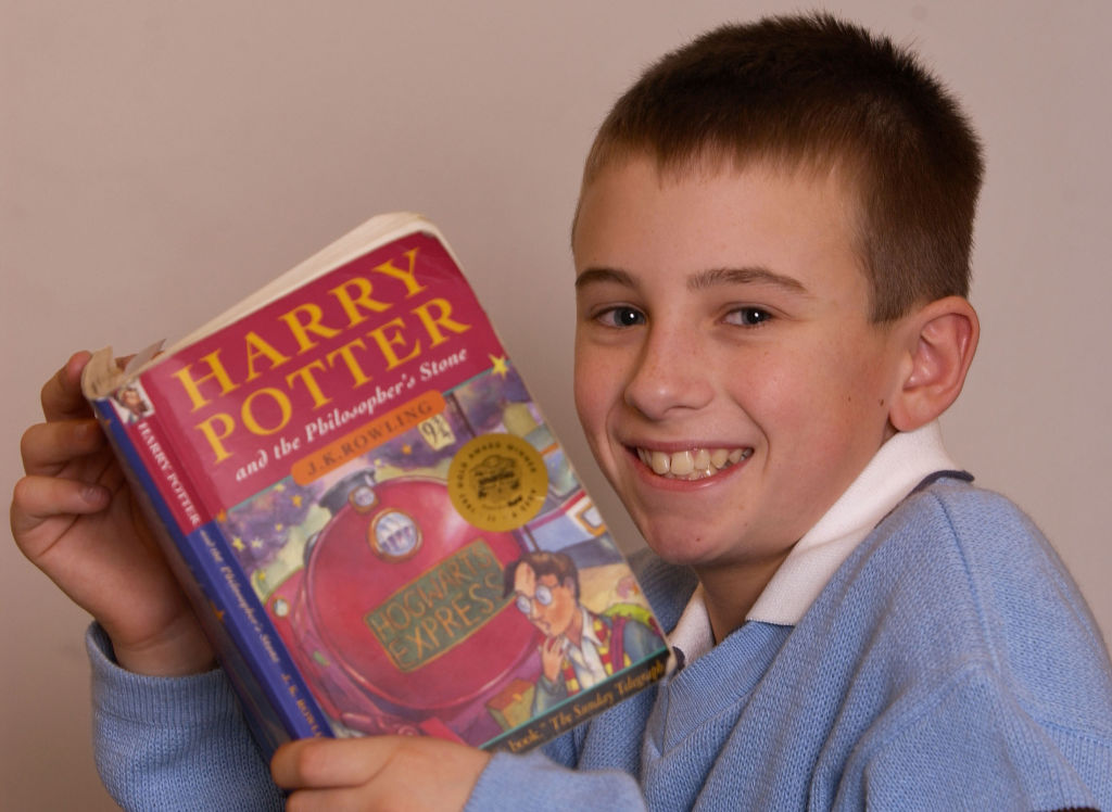 young boy smiling and holding harry potter book