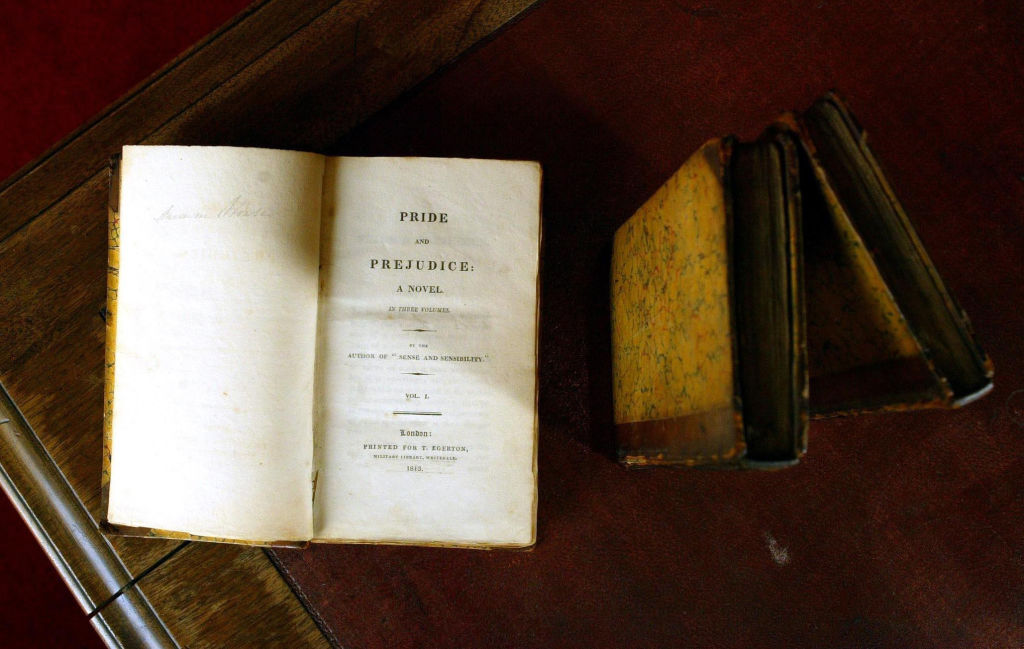 pride and prejudice early copy opened on a wooden table next to two old books