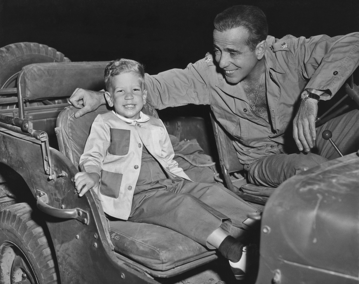 American actor Humphrey Bogart (with his son Stephen in a jeep on the set of the 1953 film 'Battle Circus'