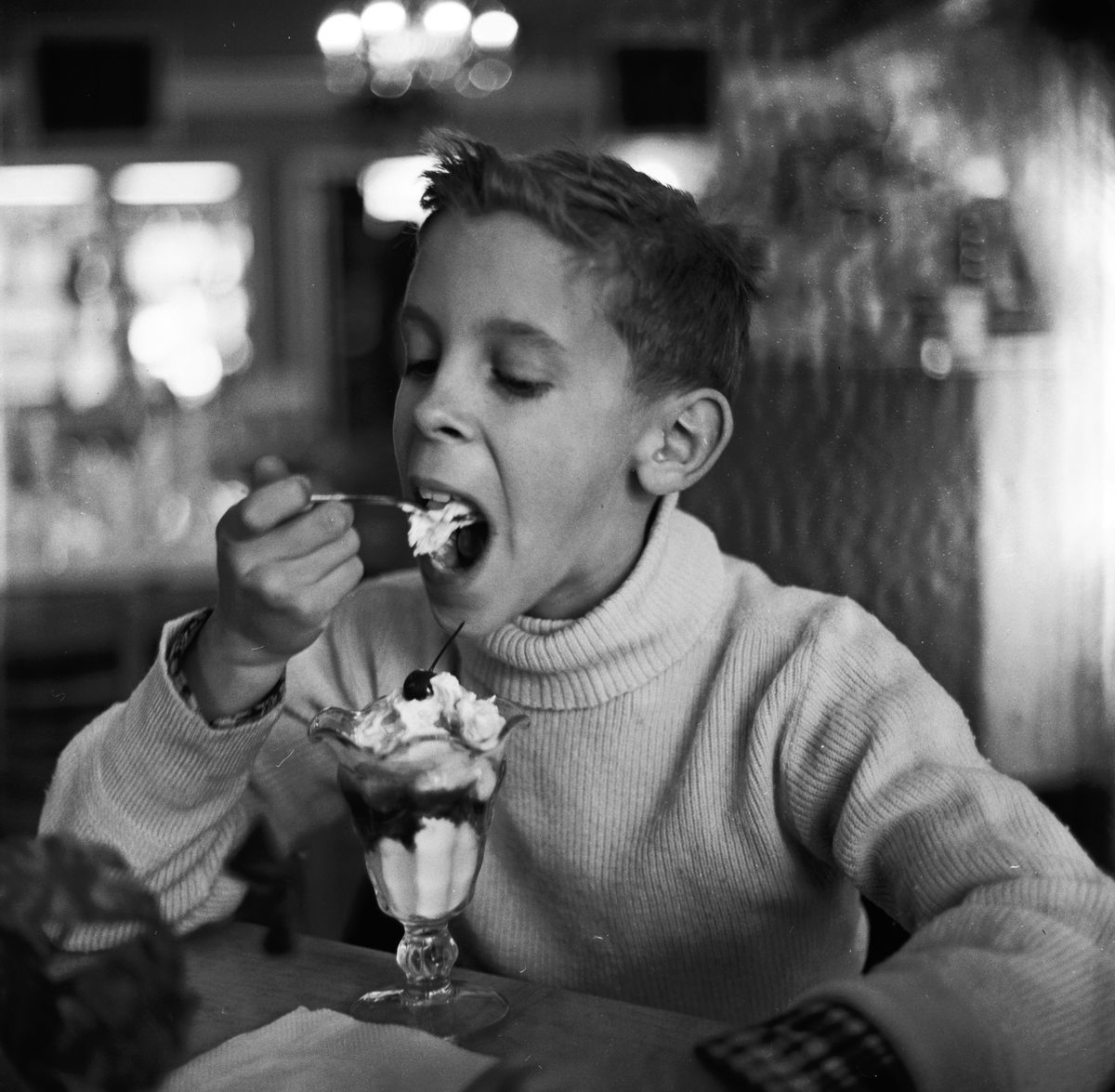circa 1955: A boy enjoys an ice cream sundae during a break from shopping. 