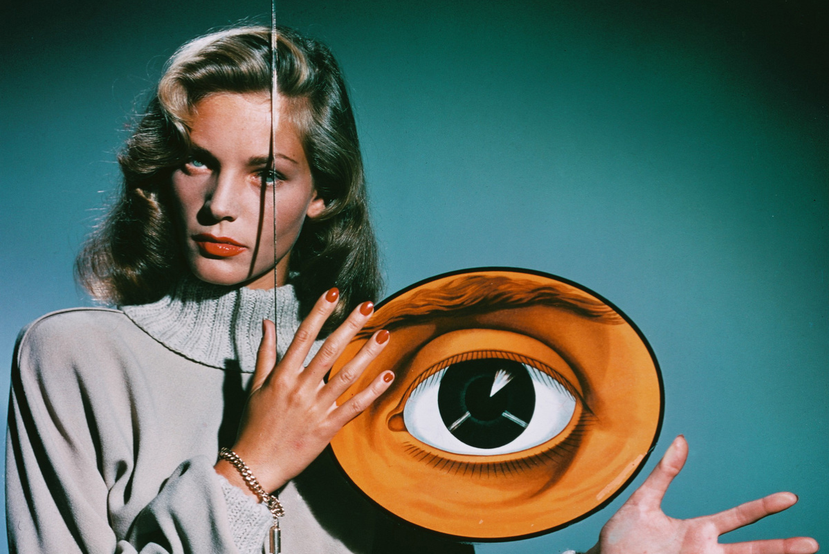 American actress Lauren Bacall poses behind a pane of glass decorated with two giant eyes, circa 1950.