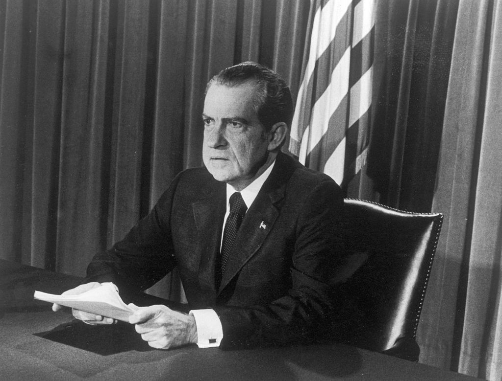 U.S. President Richard M. Nixon sits at a desk, holding papers, as he announces his resignation on television, Washington, D.C.
