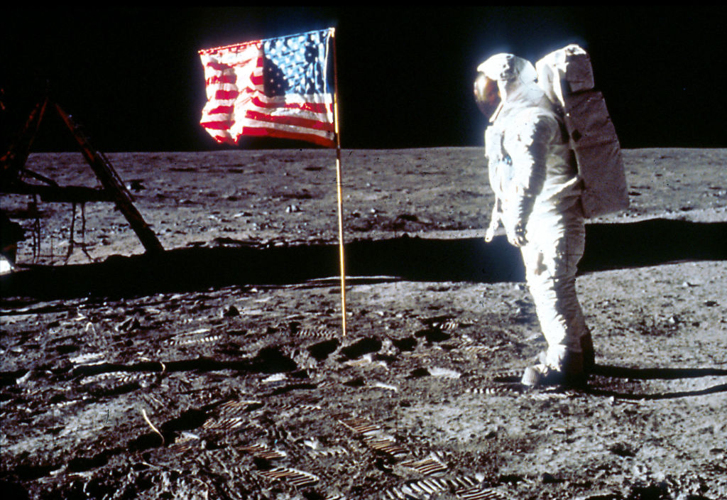 buzz aldrin in a space suit standing on the moon with a backwards american flag