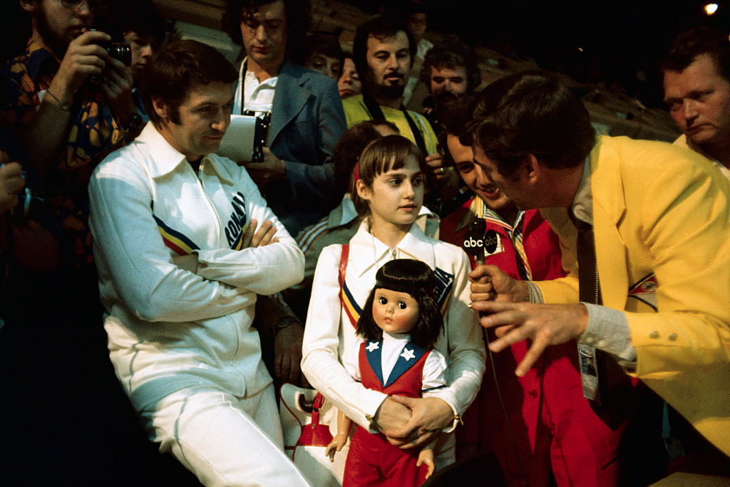 nadia comaneci holding a doll while being interviewed at the olympics