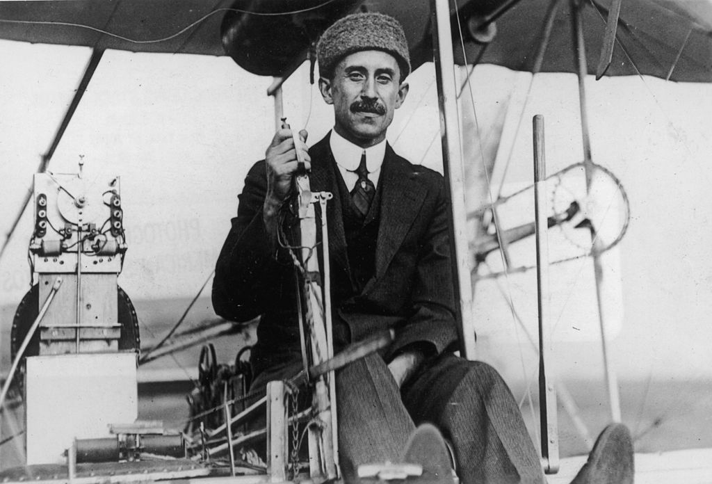 orville wright sitting in one of his biplanes dressed in a three-piece suit and a cap