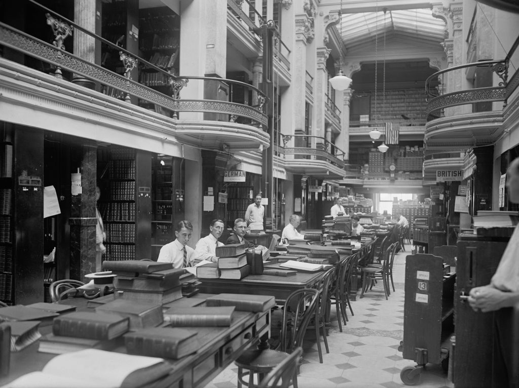 men sitting in the us patent office with large books on the tables