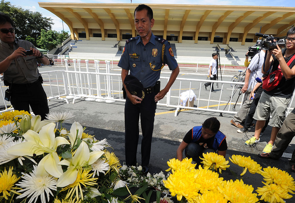 A Philippine chief inspector removes his hat while looking on to the ceremony held for victims of the bus hijacking.