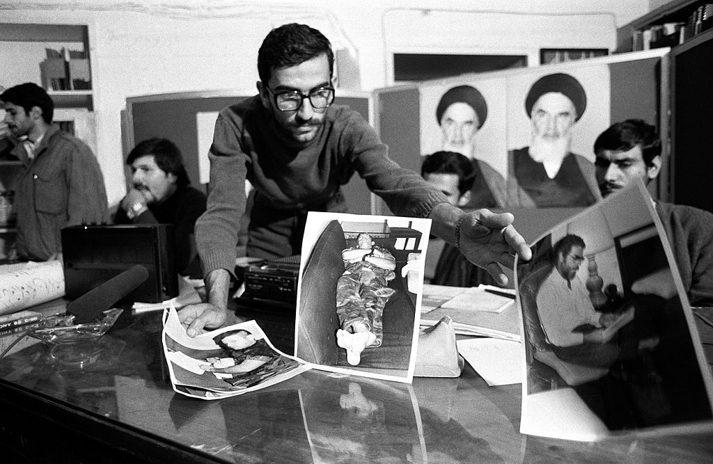 One of the invaders holds out photographs of his hostages.