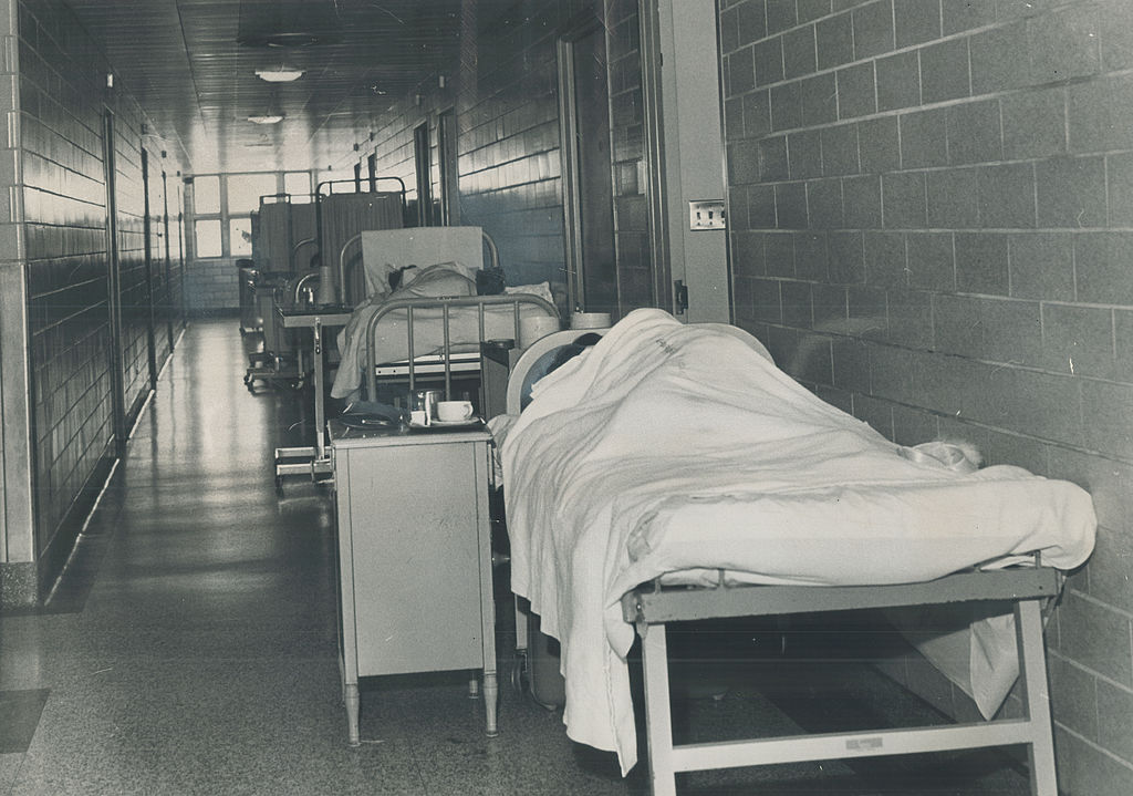 Patients rest in beds along a maternity ward hall.
