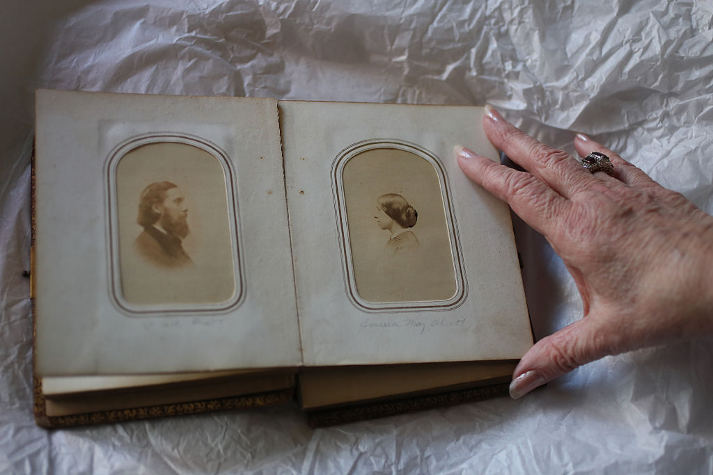 An old Alcott family photobook is held open to reveal a portrait of John Bridge Pratt facing a separate portrait of Anna Alcott Pratt.