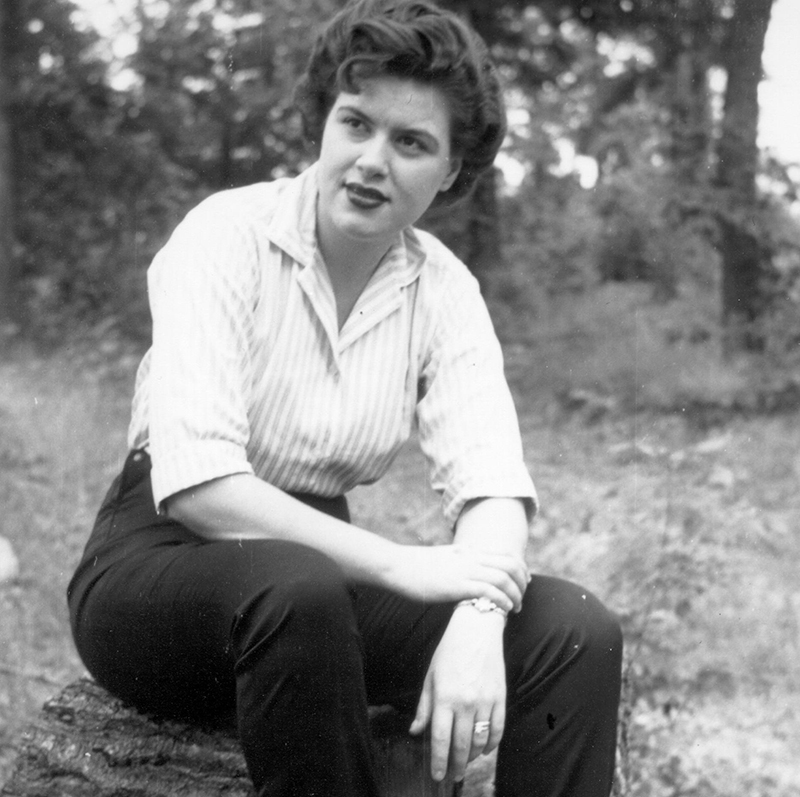 A candid photo shows Patsy sitting on a rock in the woods