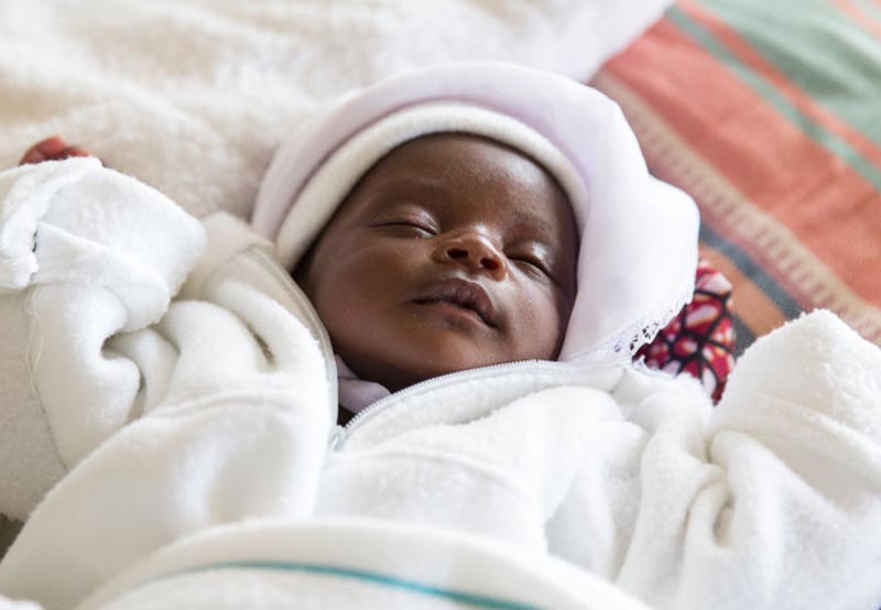 A baby sleeps in a soft, white sweater.