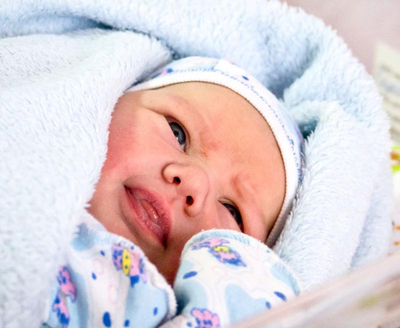A baby sticks its tongue out between its lips.