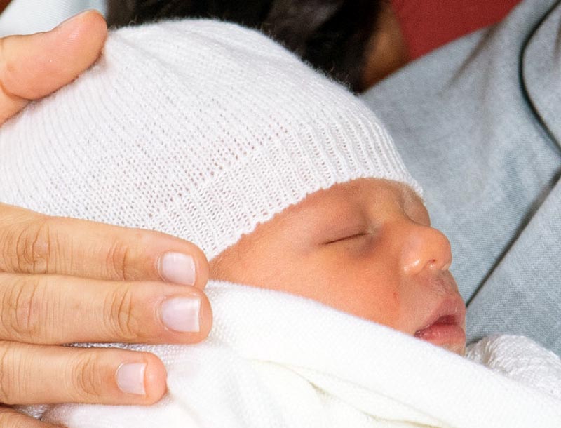 An adult hand rests on the head of a sleeping baby.