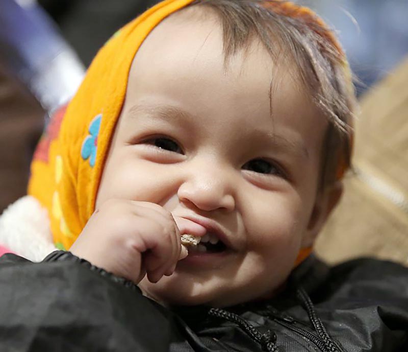 A baby smile while taking a bite of something.
