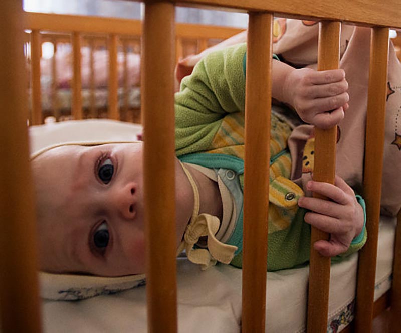 A baby peers through its crib.