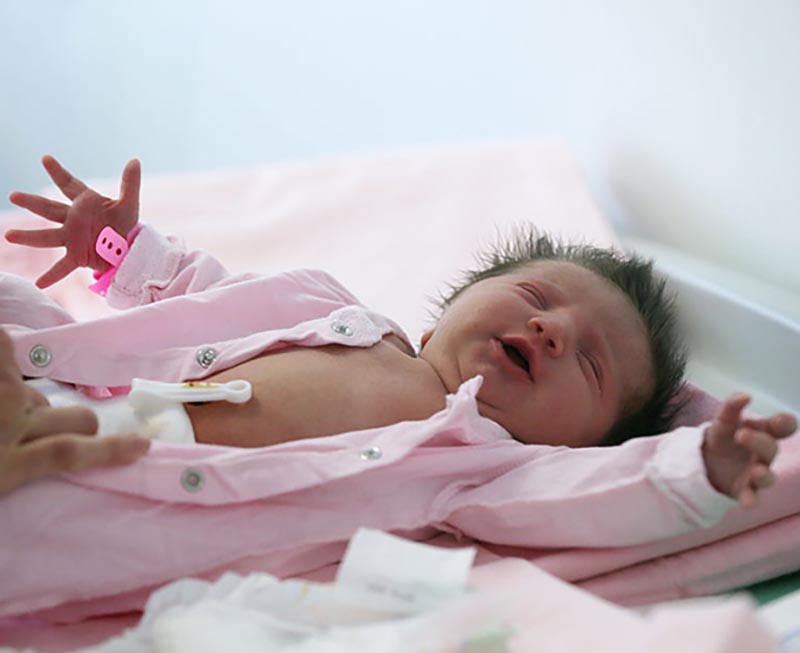A baby lays on its back with its arms out while being dressed.