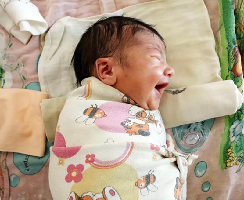 A baby with closed eyes wears a large smile.