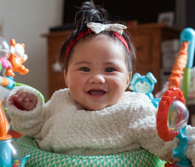 A baby smiles while standing in a jumper.