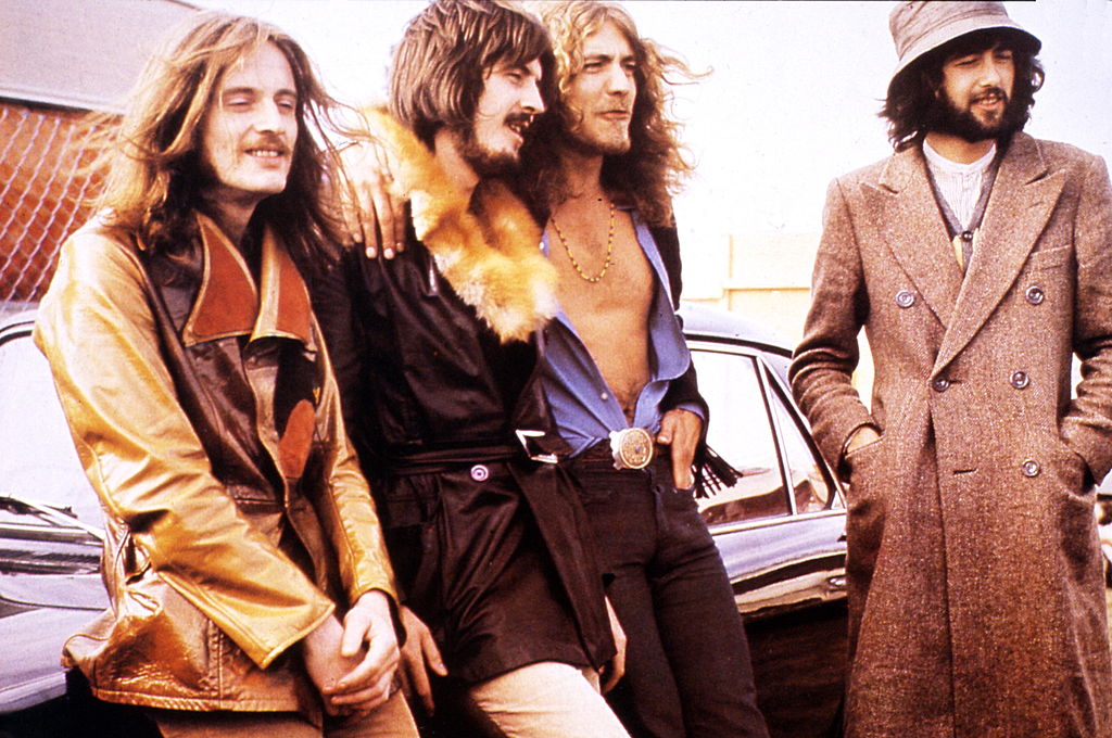 led zeppelin band members sitting in front of a car in 70s wardrobe