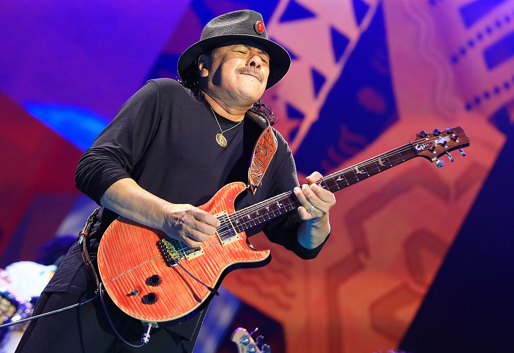 santana playing the guitar on stage and wearing a hat