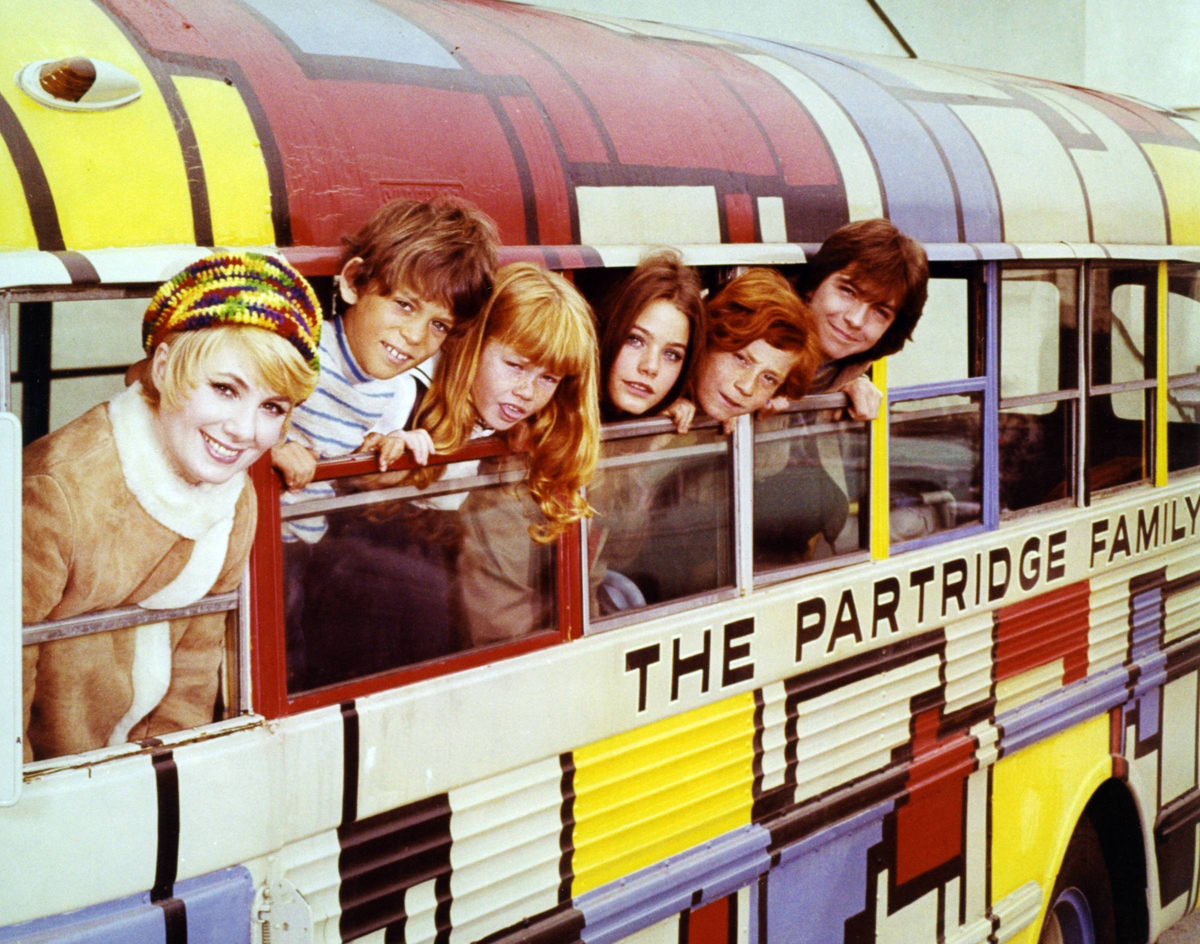 Actors of The Partridge Family lean out of the windows of their bus.