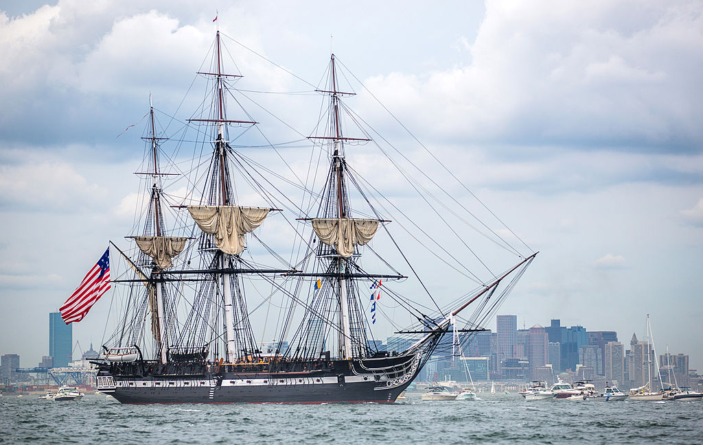 The USS Constitution sales past an urban setting.
