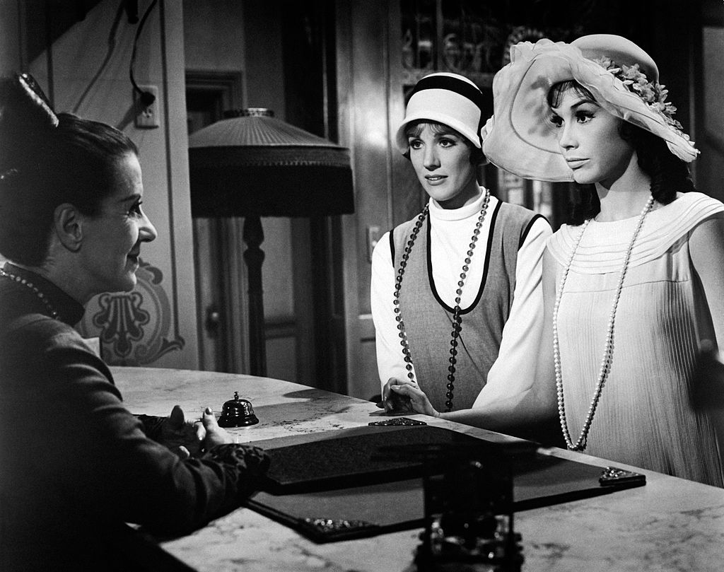 Julie Andrews and Mary Tyler Moore stand at a reception desk performing a scene in a movie.