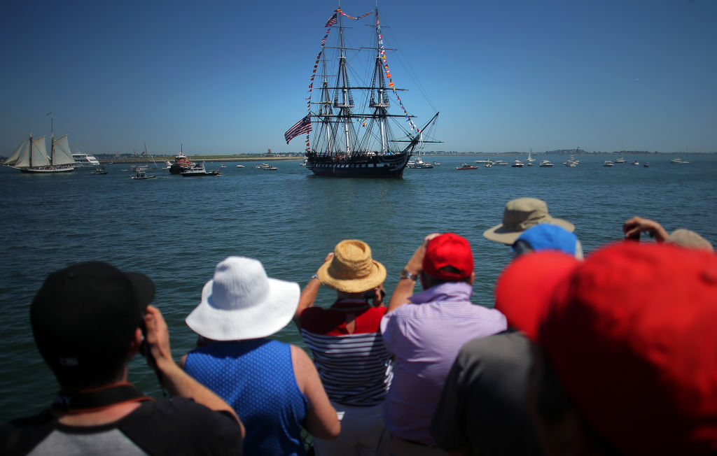 A crowd watches the USS Constitution out at sea.