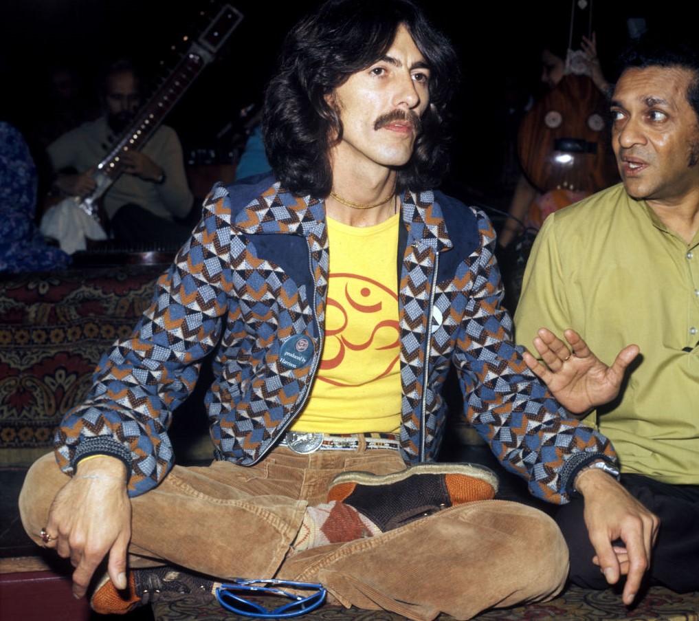 George Harrison wears a namaste shirt while sitting with his legs folded.