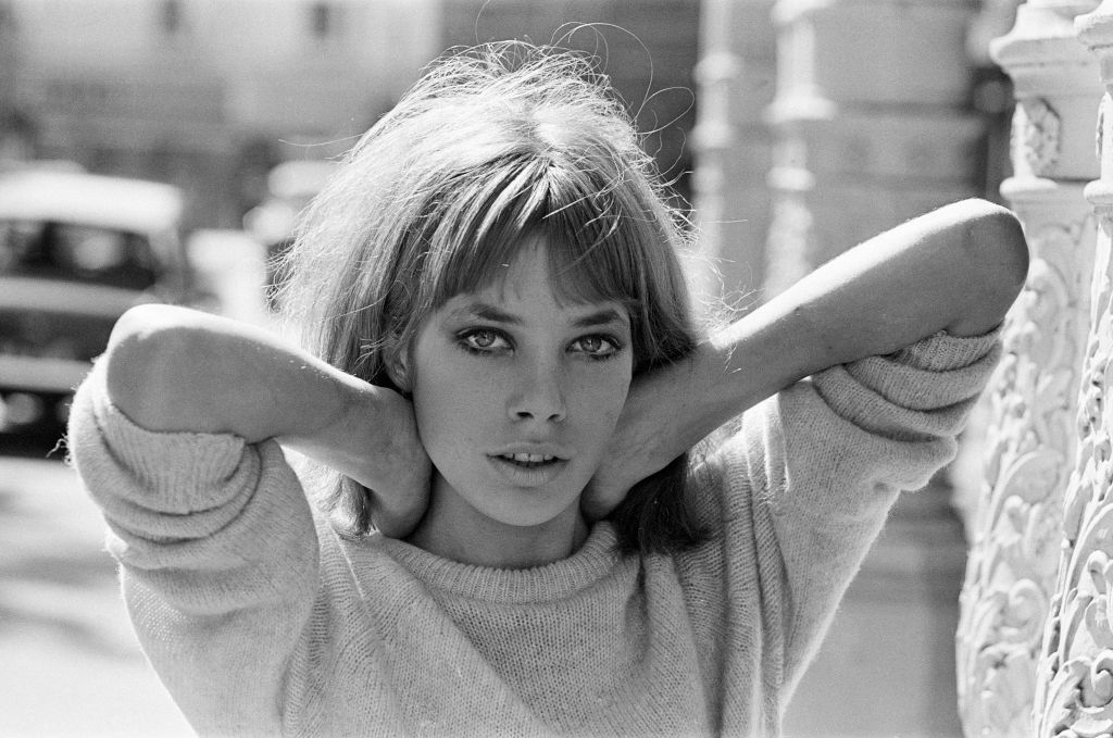 Jane Birkin poses for a black and white portrait taken on a city sidewalk.