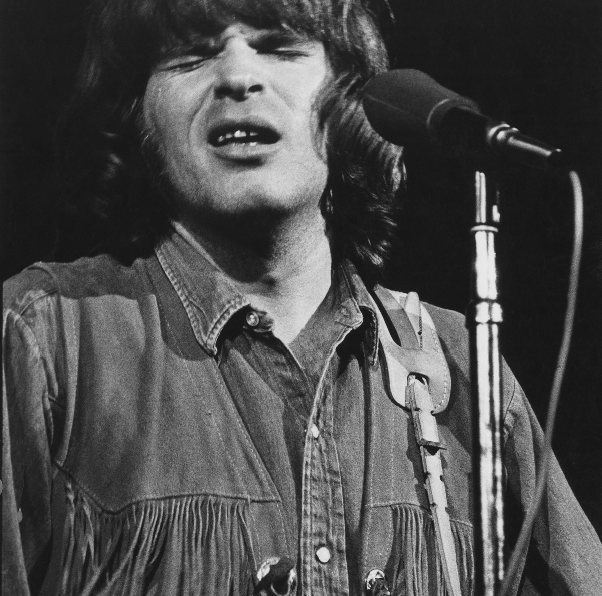 John Fogerty sings into a microphone onstage.