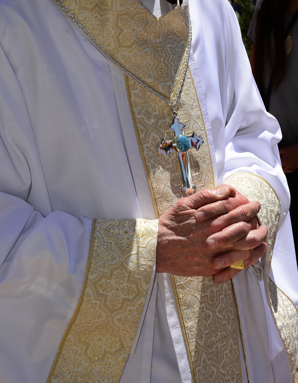 An Archbishop who wears a cross necklace folds his hands over his stomach.