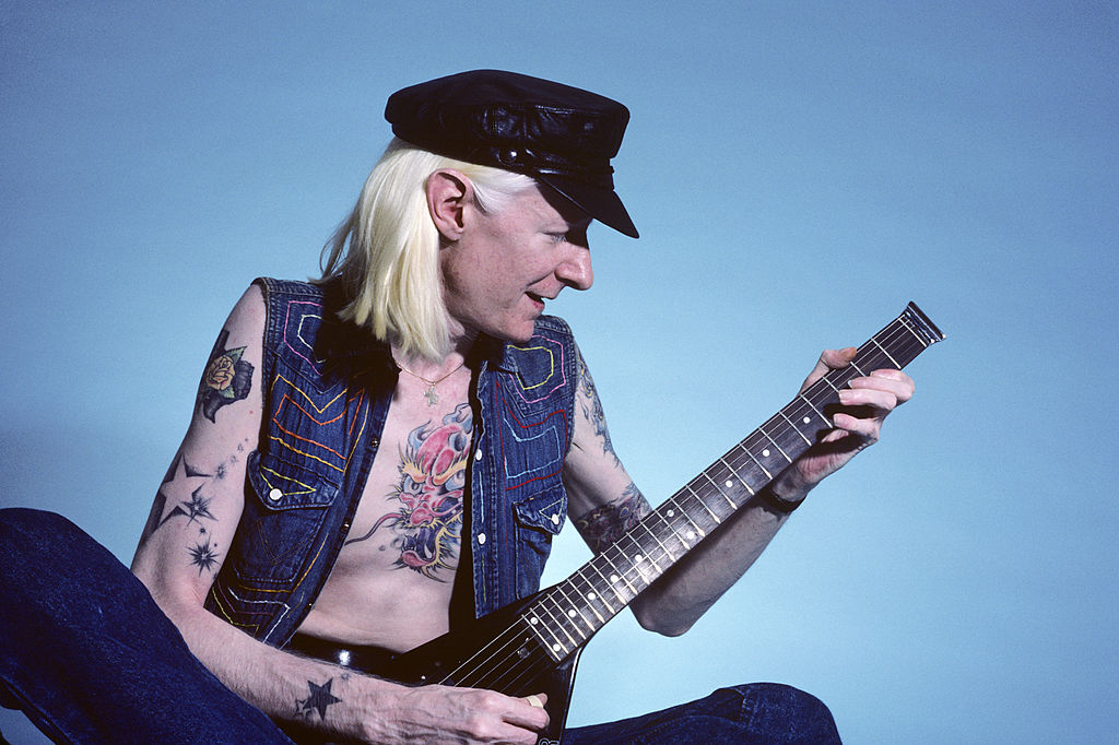 Johnny Winter plays his guitar in front of a blue backdrop during a photoshoot.