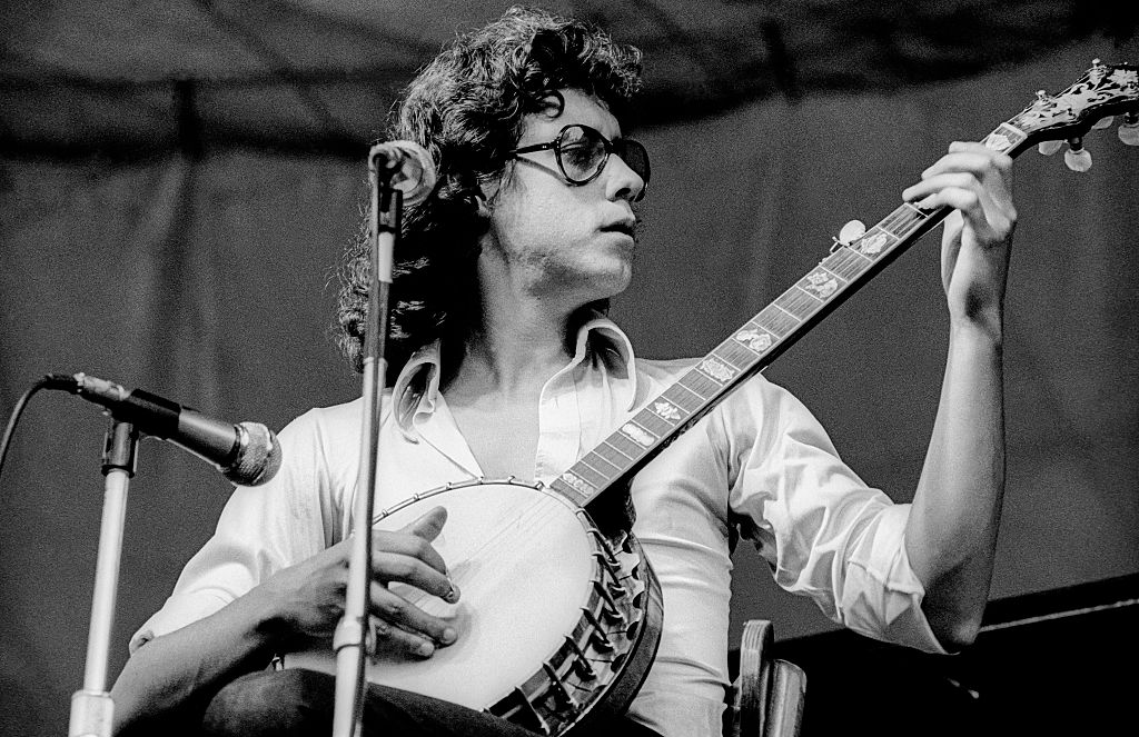 Arlo Guthrie plays a banjo onstage.