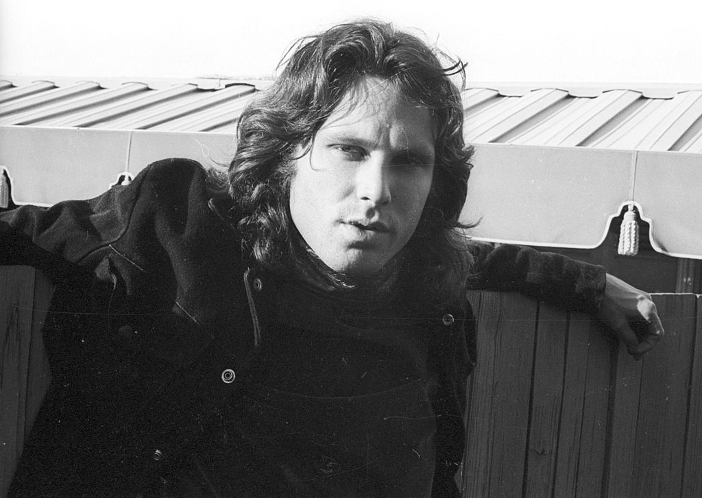 Jim Morrison poses next to a wooden fence.
