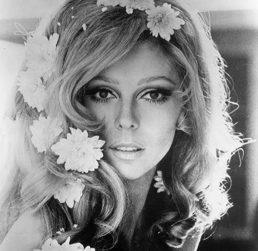 Nancy Sinatra wears flowers in her hair while looking into the camera.