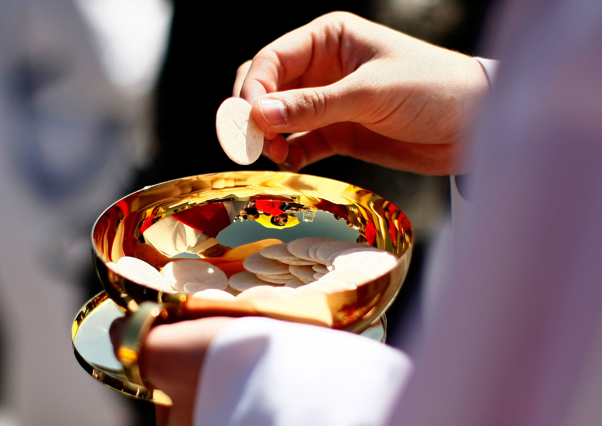 A priest holds a bowl of Holy Communion wafers.