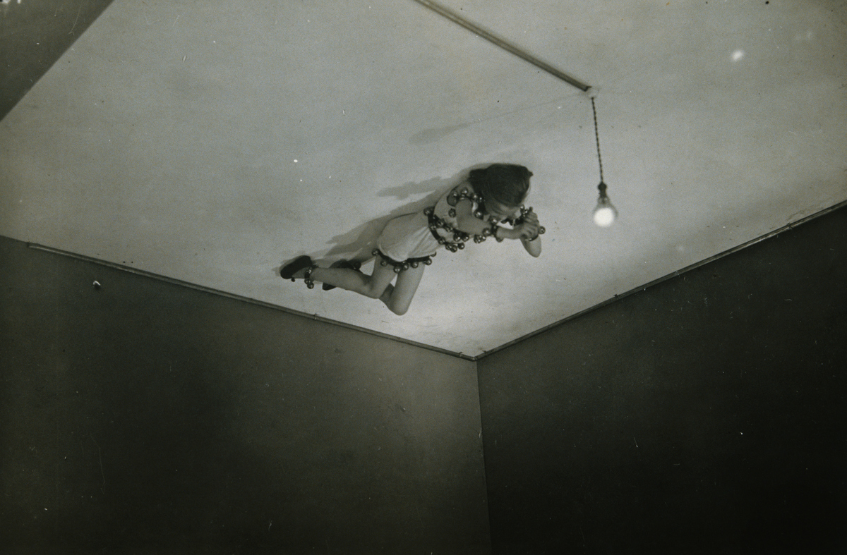 A young actress lies on the ceiling near a single light bulb in Jean Cocteau's experimental theatre.