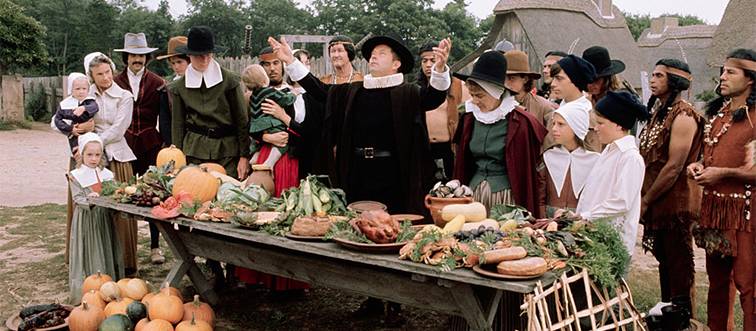people dressed as pilgrims and native americans with a table of food
