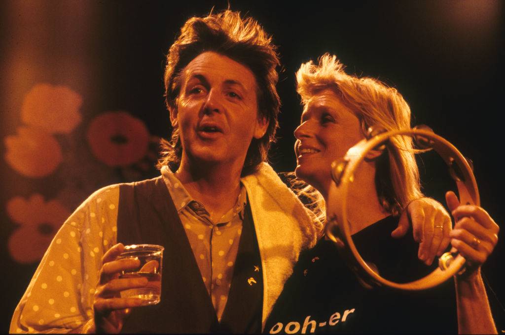 Linda holds a tamborine in one hand while posing with paul.