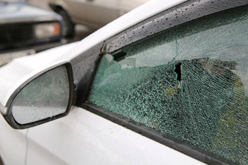 A broken car window in aftermath of a windstorm. Strong winds have damaged roofs, blown down trees and billboard posters.