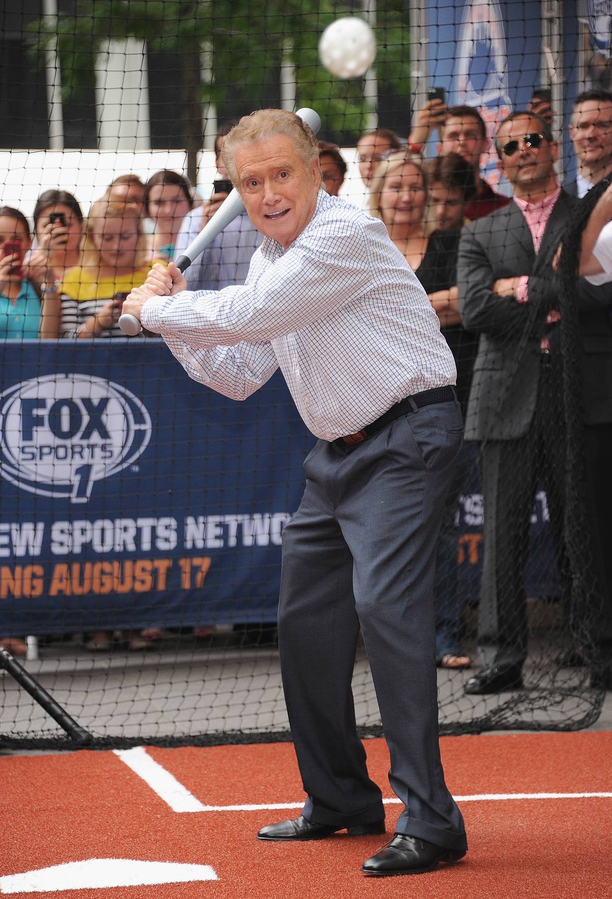 Regis Philbin is about to bat on a baseball field.