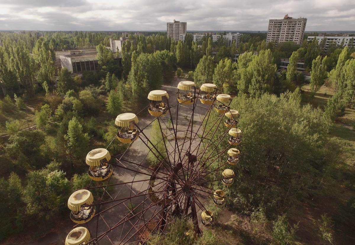 In this aerial view an abandoned ferris wheel stands on a public space overgrown with trees in the former city center