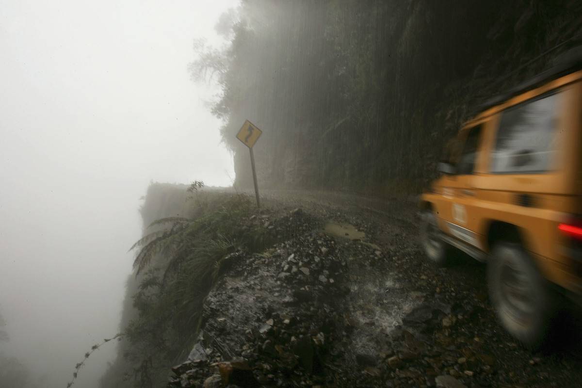 A car travels thin road on mountain side with nothing protecting from edge